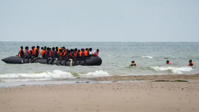 Small boat on the beach with some migrants in life jackets in the shoreline