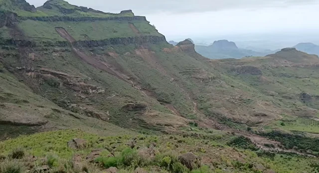 Photo showing the aftermath of a landslide in a mountainous area of western Sudan, with group of people gathered at the bottom of a landslide in the bottom right of the photo