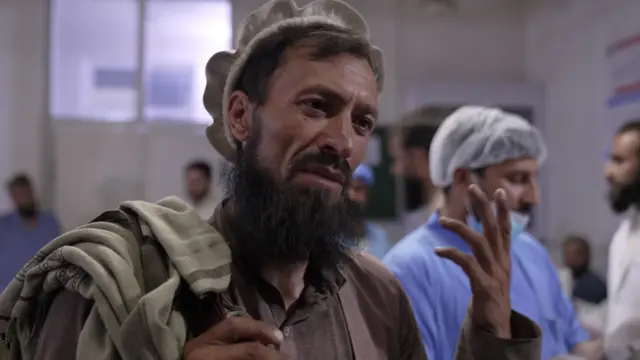 A bearded Afghan man raising his hand mid-conversation
