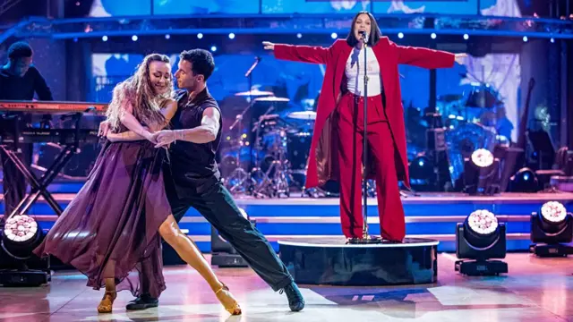 Jessie J sings on a podium as two professional dancers dance next to her