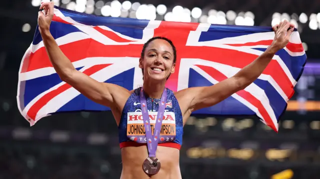 Katarina Johnson-Thompson holding a flag aloft while wearing a bronze medal