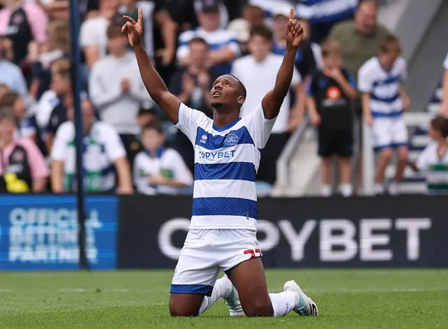 Richard Kone kneels down on the turf and points up to the sky after scoring for Queens Park Rangers