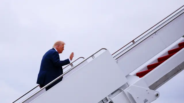 Trump on the stairs up to the doors of the plane. He waves but looks ahead
