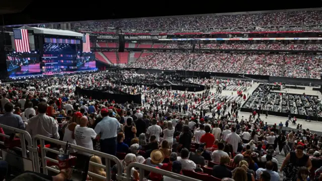 O interior do estádio, com milhares de pessoas vestidas de vermelho, branco e azul em seus assentos. Um grande número também está de pé no centro do estádio, mas também há grandes espaços vazios.