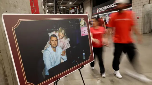 Pessoas passam por uma foto do comentarista conservador assassinado Charlie Kirk e sua esposa Erika no Estádio State Farm