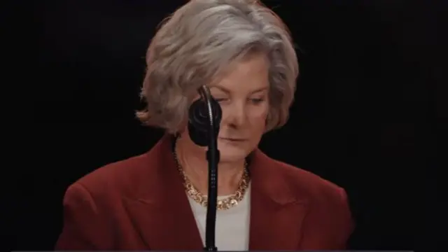 Susan Wiles olha para baixo enquanto está em frente ao microfone