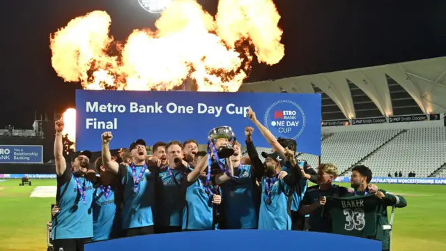 Worcetsershire players lift the One-Day Cup trophy with fire/fireworks going off behind them