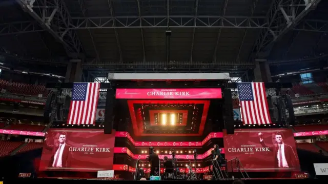 Duas bandeiras americanas foram penduradas em ambos os lados das telas em vermelho com os dizeres "Em memória de Charlie Kirk 1993-2025".