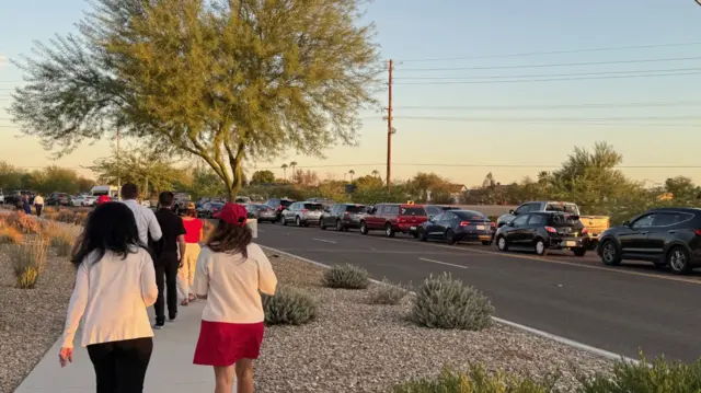 A few pedestrians walk alongside a long traffic queue