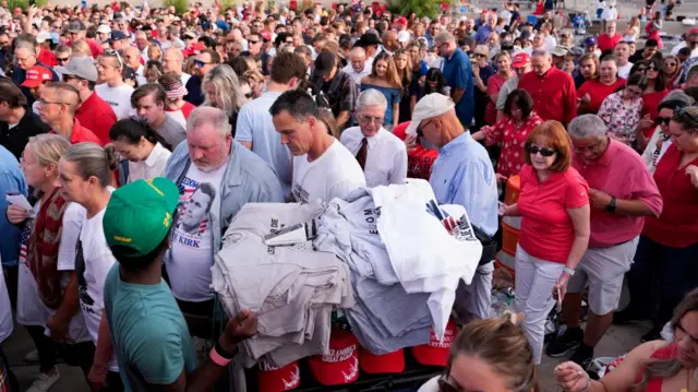 Um homem oferece mercadorias para venda enquanto as pessoas fazem fila do lado de fora para comparecer ao serviço memorial do comentarista conservador assassinado Charlie Kirk no State Farm Stadium