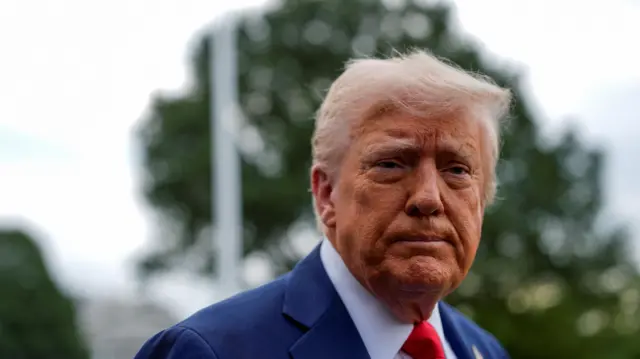 A headshot of President Donald Trump who looks towards the camera solemnly