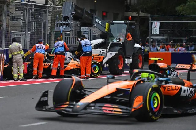 Lando Norris drives past Oscar Piastri's crashed car