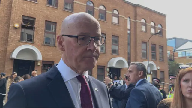 John Swinney pictured wearing a suit and burgundy tie. He is a bald man who wears glasses.