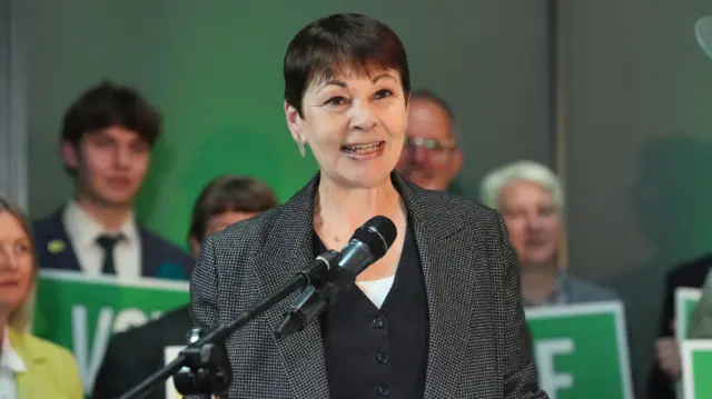 Caroline Lucas stands at a lectern speaking to the public