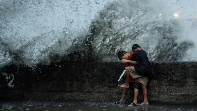 Two boys take cover from high waves slamming onto a sea wall in the Philippines