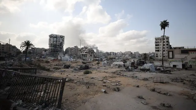 A cloud of white smoke emerges from a burning building in the far background after an air attack on Gaza City. Heavily damaged buildings and tents in the foreground