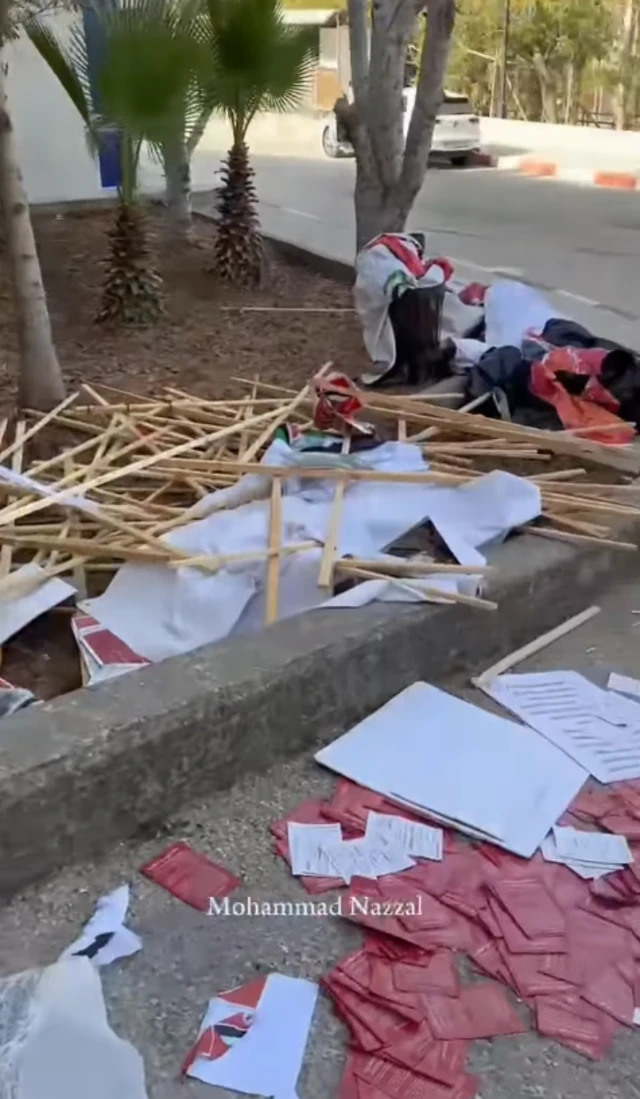 A screenshot of a video showing wooden poles, posters and clothing strewn across a pavement