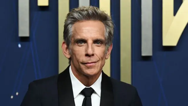 Actor Ben Stiller smiles in a dark suit and white shirt as he walks the red carpet at the Primetime Emmy Awards