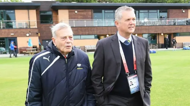 Dickie Bird and Mark Arthur walk on a cricket ground.