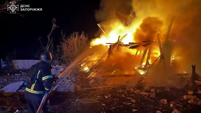 A firefighter puts a large fire out above a demolished building