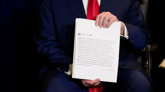 A close up of some hands holding a print-out of a social media post from President Trump endorsing Milei