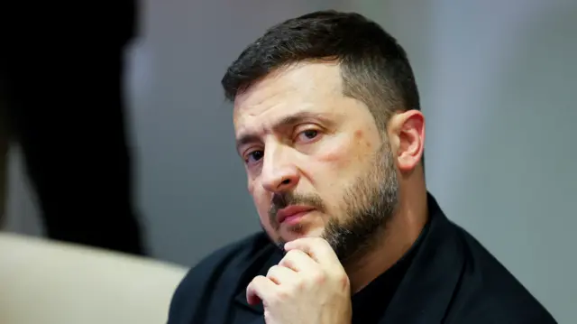 Zelensky in a black jacket in front of a grey wall