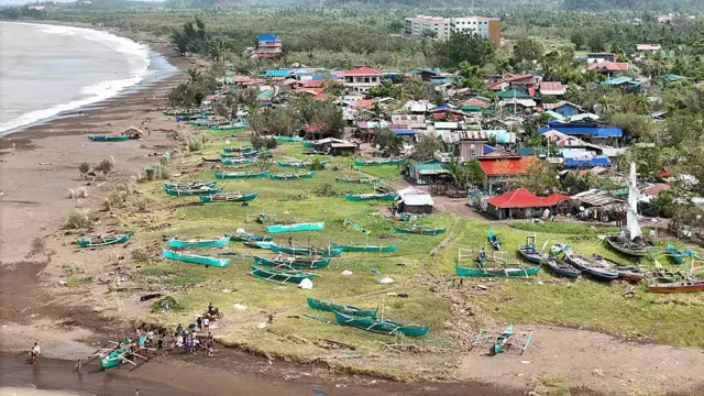 Damaged boats stranded on a field near houses by a beach