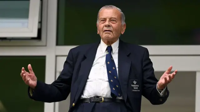 Dickie Bird, who wears a suit and tie, holds up his hands in frustration.