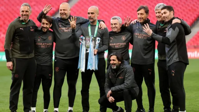Pep Guardiola and his coaching staff gesture the number 4 with their hands to signify their fourth carabao cup victory in a row.