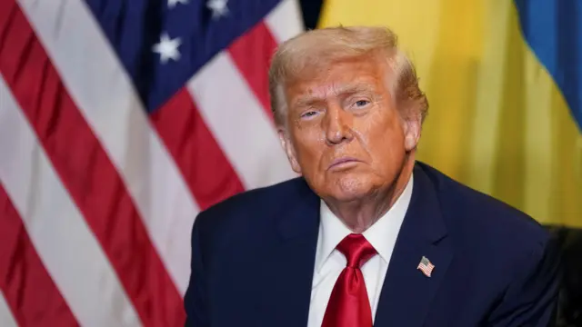 Trump sits in front of Ukrainian and US flags