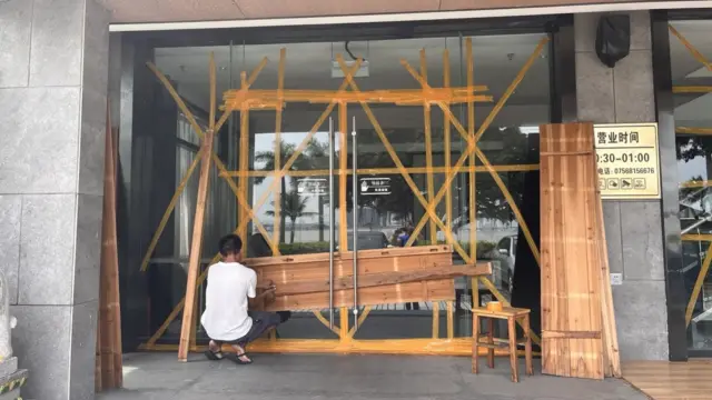 A store owner has taped up the main entrance of his store and is placing wooden planks across it