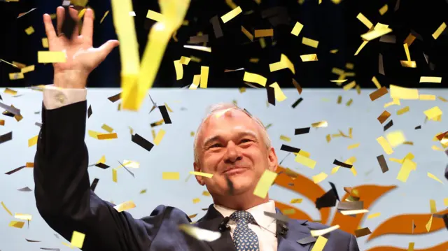 Liberal Democrat Leader Ed Davey waves as yellow confetti falls around him