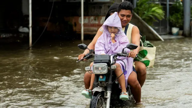 Two adults and a child riding a motorcycle on a flooded street