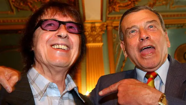 Dickie Bird (R) gestures towards Rolling Stones band member, Bill Wyman, who smiles next to him.