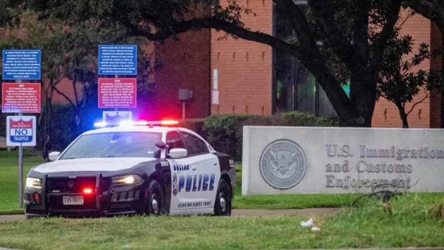 A Dallas police car with lights flashing sits outside ICE building entrance