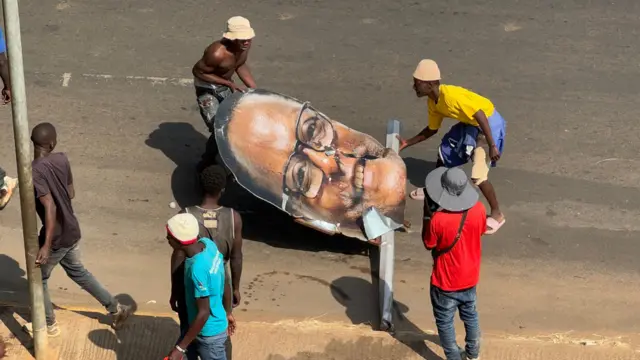 Two men carry a huge a larged, detached photo of Lazarus Chakwera's head