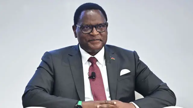 Chakwera sits with his hands clasped, wearing a suit and glasses