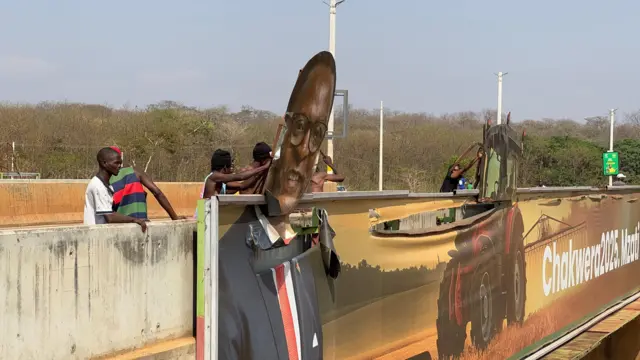 Men attempt to pull the rip Lazarus Chakwera's head off of a large poster of him