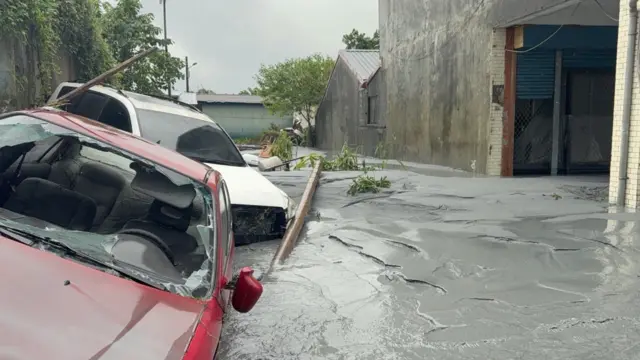 Two damaged cars (one red and one white) float in the grey floodwater in Guangfu Township, Hualien