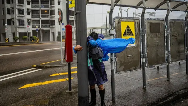 A woman holding onto a lamp post at a bus stop