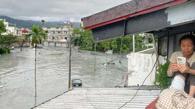 Woman seeking cover from floods on the roof of a house tinkers with her mobile phone