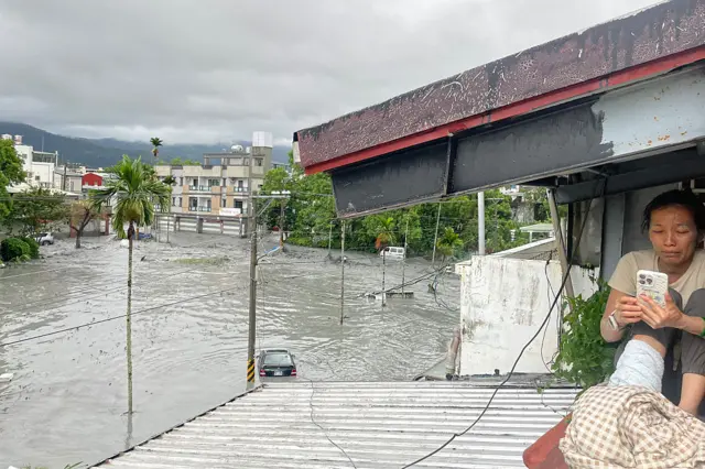 A resident uses her mobile phone while sitting on the roof of a house, as water from a burst landslide dam overflows and floods the area in Hualien on September 23, 2025, as a result of heavy rain due to Super Typhoon Ragasa.