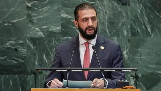 A man in a blue suit and red tie at a podium