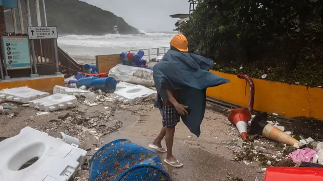 A man in a yellow construction helmet walks around debris