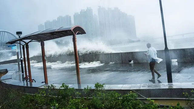 A man walks along a path bordering waters in Hong Kong, as waves splash over the wall