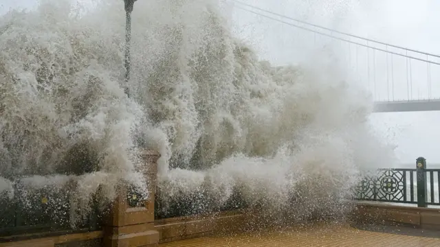A huge wave breaks on a railing and lamp post