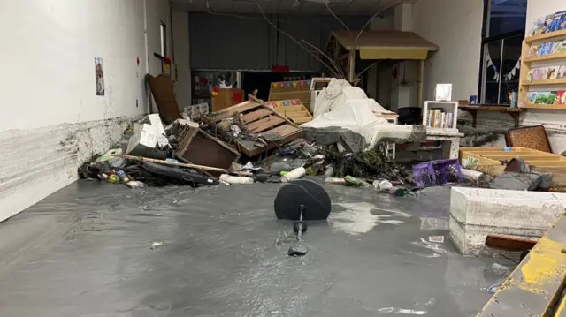 A bookshop drenched in mud, with a few collapsed bookshelves and other furniture