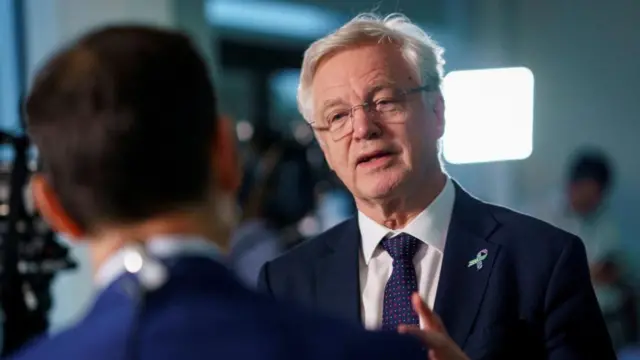 A man in a dark navy suit speaks in a low lit room