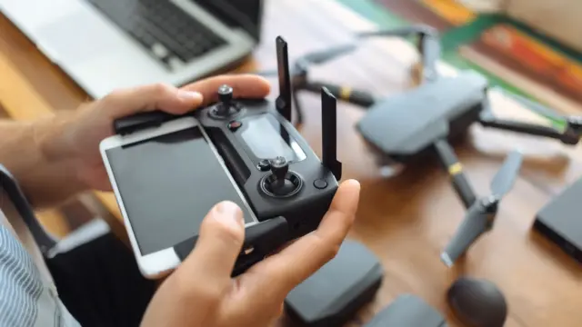 Cropped hands of engineer using mobile phone with remote control in office