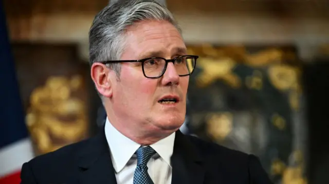 Close up of Keir Starmer mid-speech in a black suit, white shirt and patterned blue tie